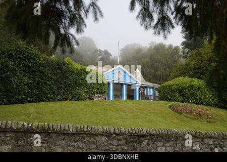 Cottage blu nel pozzo di St Ronan, annidato tra il verde e un muro di pietra in un giardino nebbioso. Foto Stock