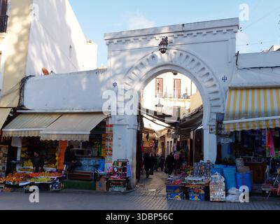 Elegante porta della Medina accanto a negozi con tende da sole a Tangeri, Marocco. 17 dic. 2025 Foto Stock