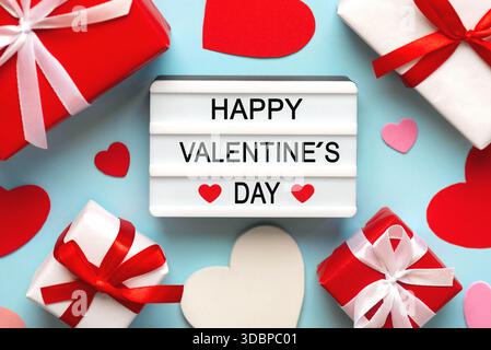 Scatola luminosa con la parola buon San Valentino accanto ai cuori e scatole regalo su sfondo blu. Concetto di San Valentino Foto Stock