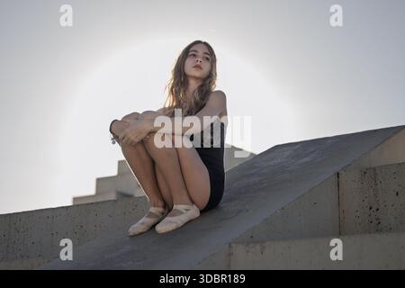 Una ragazza di 12 anni seduta su una moderna struttura in cemento all'aperto durante l'ora d'oro Foto Stock