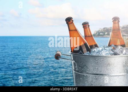 Birra in secchio metallico con ghiaccio vicino al mare. Drink estivo rinfrescante Foto Stock