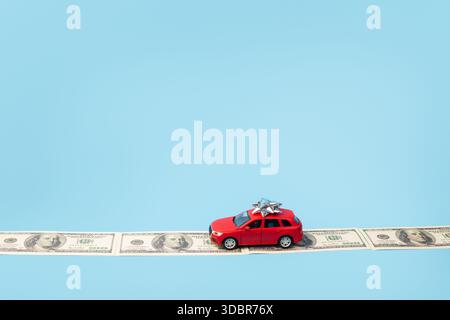 auto giocattolo rossa sulla strada dei soldi isolata su sfondo blu Foto Stock