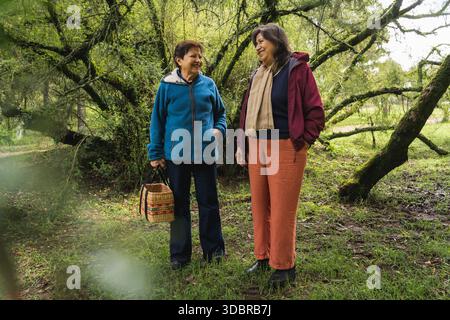 Due amiche che sorridono si divertono a conversare mentre camminano in una foresta all'aperto Foto Stock