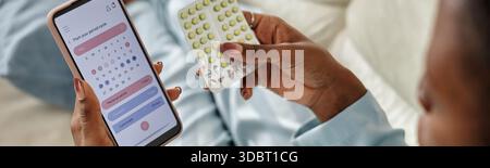 Giovane donna nera che controlla le pillole anticoncezionali utilizzando l'app per smartphone Foto Stock