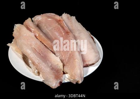 filetto di nasello crudo fresco su piatto bianco su sfondo nero Foto Stock