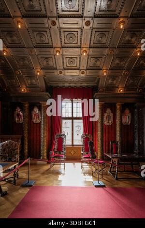 Sigmaringen, Germania - 09 settembre 2025: La vista dell'interno del castello di Hohenzollernschloss rivela intricate incisioni sul soffitto, regali drappi rossi e sole Foto Stock