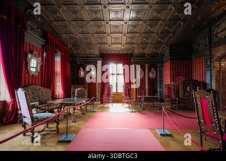 Sigmaringen, Germania - 09 settembre 2025: Veduta della sontuosa sala del castello di Hohenzollernschloss, dove i drappi di rubino cadono contro pareti ornamentali scolpite Foto Stock