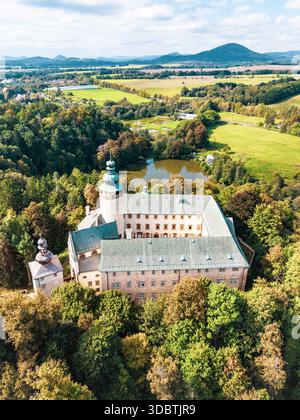La vista dall'alto del castello di Lemberk mostra la sua architettura storica annidata tra alberi vibranti e un paesaggio sereno. I campi vicini e un laghetto si aggiungono al pittoresco paesaggio. Foto Stock
