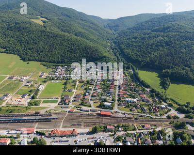 Vista aerea di un insediamento annidato alla base di montagne verdeggianti, con edifici raggruppati intorno a una ferrovia, Margecany, regione di Kosice, Slovacchia. Foto Stock