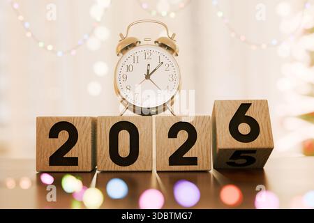 Conto alla rovescia per l'anno nuovo 2026. Una sveglia si trova sui blocchi numerici in legno, simboleggiando l'anno prossimo e la scadenza per gli obiettivi. Luce colorata festosa Foto Stock