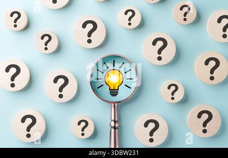 Trovare soluzioni tra le domande. Punti interrogativi su sfondo blu, mentre la lente d'ingrandimento mette a fuoco le lampadine incandescenti, alla scoperta di soluzioni innovative Foto Stock