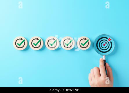 Raggiungimento degli obiettivi aziendali e concetto di controllo della qualità. La lente di ingrandimento evidenzia il bersaglio a forma di freccia e i segni di spunta verdi che simboleggiano la precisione e il successo Foto Stock