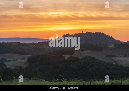 Vista di un villaggio toscano arroccato sulla cima di colline ondulate bagnate dal caldo bagliore del tramonto, che getta ombre morbide sul paesaggio, Montepulciano, Tusca Foto Stock