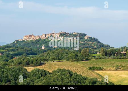 Vista della luce dorata del sole che baciano gli antichi edifici in pietra in cima alla collina, abbracciati da lussureggianti alberi verdi e colline ondulate, Montepulciano, Toscana, Ita Foto Stock