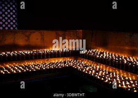 File di lampade a burro in fiamme all'interno di un tempio, che formano un caldo sfondo astratto con una luce del fuoco. Foto Stock
