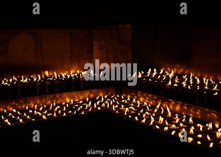File di lampade a olio scintillanti in un tempio, che creano un caldo sfondo astratto di luce del fuoco e atmosfera spirituale. Foto Stock