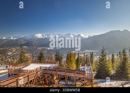 Vista mozzafiato delle montagne da una piattaforma di osservazione, cielo azzurro, alberi sempreverdi, catena innevata in lontananza. La città di Zakopane ai piedi di Foto Stock