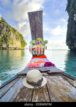 Vista di una tradizionale barca a coda lunga adornata da fiori vivaci e un cappello di sole che scivola attraverso le acque turchesi incorniciate da torreggianti scogliere calcaree, pH Foto Stock