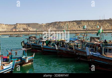 Vista delle barche da pesca che rimbalzano dolcemente nel porto, delle bandiere che sventolano nella brezza sullo sfondo di scogliere scoscese, Gwadar, Balochistan, Pakista Foto Stock