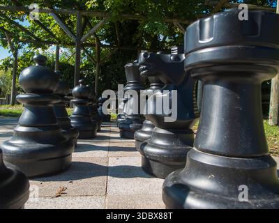 Visuale grandangolare bassa dei pezzi degli scacchi sistemati in una partita a scacchi all'aperto sotto un pergolato. Foto Stock