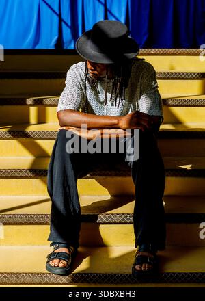 Una persona che indossa un cappello e un sandalo siede su una scala gialla. Foto Stock