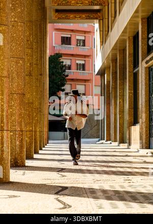 Un uomo con dreadlock che indossa un cappello e una camicia con bottoni corre verso la fotocamera. Foto Stock