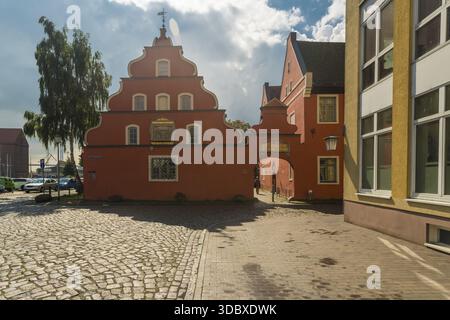 Vista di un edificio rosso vivace con un'architettura unica si erge orgogliosamente su ciottoli, un portale per la storia sotto un cielo luminoso, Stralsund, Meclemburgo- Foto Stock