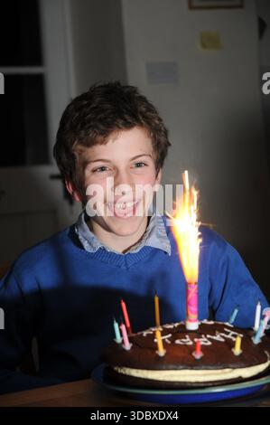 Un bambino sorridente festeggia un compleanno a casa con una torta e una candela sparkler illuminata, godendosi un momento felice in famiglia all'interno. Foto Stock