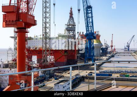 La vista delle imponenti gru rosse e blu incombe sulla massiccia piattaforma petrolifera offshore in costruzione, una sinfonia di potenza industriale, Shanghai, Shangha Foto Stock