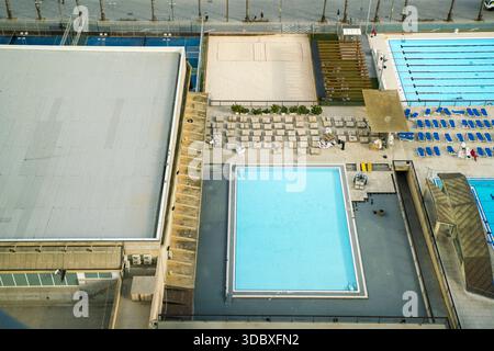La vista di una scena vibrante si dispiega con piscine di colore blu che contrastano con i campi da pallavolo sabbiosi e una vasta struttura sportiva, Barcellona, Catalon Foto Stock