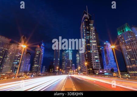 Vista delle vivaci strisce di luce che si sfocano dall'altra parte della strada, riflettendo sui grattacieli torreggianti che piergono il cielo blu profondo, Dubai, United AR Foto Stock