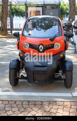 LUGANO, SVIZZERA, 06.20.2025: Vista frontale ravvicinata di una piccola Renault Twizy arancione parcheggiata in un parcheggio soleggiato. Riflessi di alberi sul windshi Foto Stock