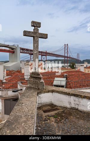 Croce in pietra antica su una terrazza sul tetto con vista sul Ponte 25 de Abril e sulla statua del Cristo Re a Lisbona, Portogallo. Foto Stock