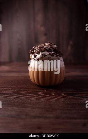 latte cremoso ricoperto da panna montata e scaglie di cioccolato in vetro a costine su un ricco sfondo di legno che crea un'atmosfera accogliente e calda con sof Foto Stock