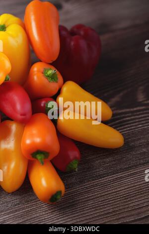 un vivace assortimento di peperoni colorati, tra cui varietà arancio, giallo e rosso, sono elegantemente disposti su una superficie rustica in legno, showcas Foto Stock