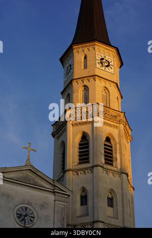 Vista dall'angolo basso dello storico campanile gotico con orologi sulla chiesa di San Michele (Michaelerkirche) a Vienna, illuminata da una calda luce occidentale Foto Stock