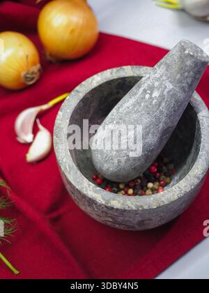 Concetto di preparazione degli alimenti con mortaio di pietra, grani di pepe, aglio e cipolla, vista dall'alto Foto Stock