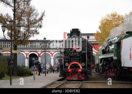Mosca, Russia - 18 ottobre 2025: Locomotive a vapore dell'era sovietica in mostra al museo ferroviario Povorotny Krug, visitatori, edifici a roundhouse Foto Stock