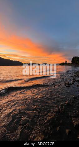 Spettacolare tramonto sul Lago Calafquén in Cile, con colori vividi blu, rosso e giallo che riempiono il cielo e si riflettono sulle calme acque del lago. Foto Stock