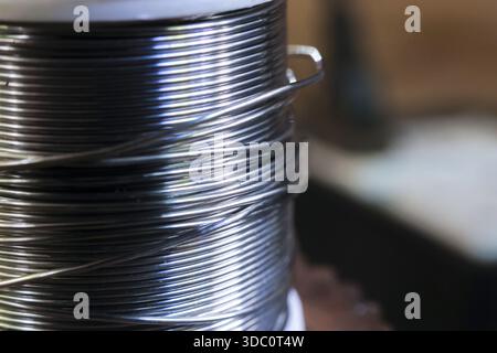 Vista ravvicinata del filo conduttore di saldatura argentato avvolto sulla bobina che mostra la trama dettagliata del materiale metallico lucido pronto per i lavori di riparazione elettrica e industria Foto Stock