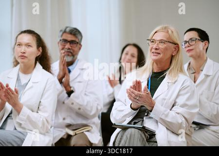 Gruppo di medici di mezza età e anziani che applaudono durante il seminario medico Foto Stock
