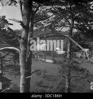 Bohorodychne, regione di Donetsk, regione di Sloviansk, RSS Ucraina, URSS, 1960 anni Una fotografia di paesaggio d'archivio scattata da una collina boscosa. La vista guarda attraverso i tronchi di pini in primo piano per rivelare un gruppo di case rurali nella valle. I cottage del villaggio sono circondati da giardini. L'immagine utilizza l'inquadratura naturale per catturare l'atmosfera appartata e serena della campagna. Uno sguardo nostalgico sulla vita quotidiana e sulla natura delle tranquille Donbas. Foto Stock