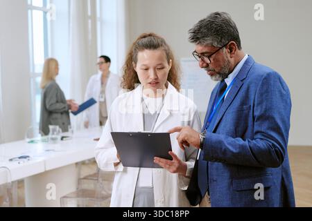 Uomo di mezza età e giovane donna asiatica adulta discutere rapporto medico Foto Stock