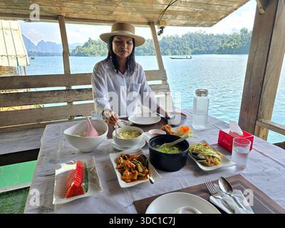 Gustando un delizioso assortimento di piatti tradizionali thailandesi, questa tranquilla scena lacustre cattura la bellezza del lago Cheow LAN a Khao Sok Thailandia. Mamma lussureggiante Foto Stock