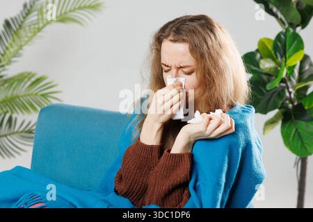 Raffreddore e influenza. Ritratto di donna malata catturati freddo, sensazione di malessere e starnuti in carta di pulizia. Primo piano della bella ragazza malata coperti in coperta Foto Stock