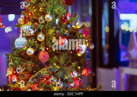 Rovigo, italia 18 dicembre 2025: Rami di alberi di natale adornati da luci accese e baubles colorati, che creano un'atmosfera calda e festosa per le vacanze Foto Stock