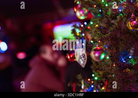 Rovigo, italia 18 dicembre 2025: Albero di natale decorato con luci colorate e ornamenti a marchio grimbergen, che riflettono una vibrante atmosfera festosa Foto Stock