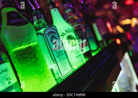 Rovigo, italia 18 dicembre 2025: Bottiglie di midori, zaffiro di bombay e liquore malibu che brillano di luce verde, simboleggiano la vita notturna, la celebrazione, un Foto Stock