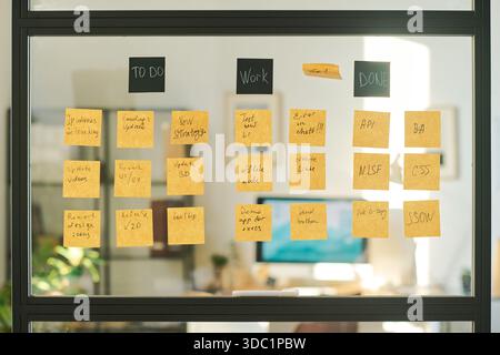 Parete di vetro coperta da appunti che mostrano cose da fare, lavorare e fare, organizzare le attività di progetto e il flusso di lavoro in un ufficio moderno, riflettendo l'utilizzo della metodologia agile o scrum Foto Stock