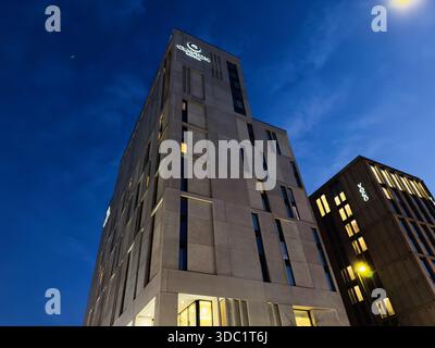 Manchester, Regno Unito - 10 dicembre 2025: Un alto edificio alberghiero di Clayton a Manchester, Regno Unito, con finestre luminose che riflettono la vita serale della città e gli affari. Foto Stock